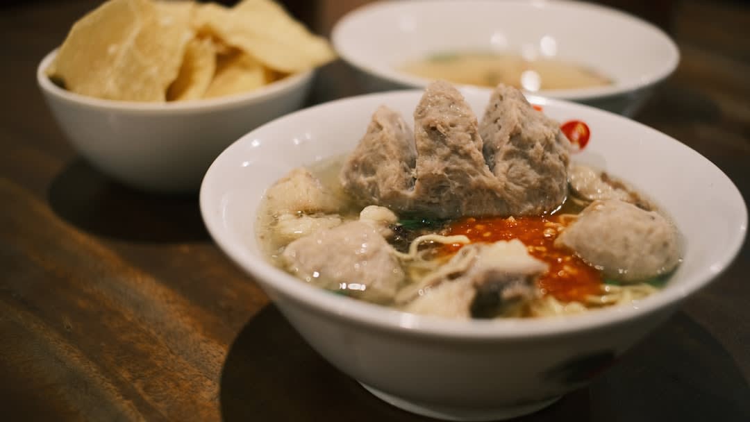 Bowl of empal gentong beef offal stew with turmeric broth and rice cakes, a Cirebon specialty