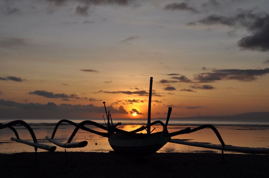 Traditional wooden outrigger boats resting on the sand at sunset