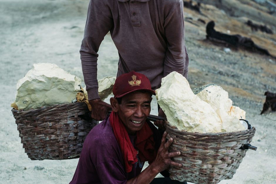 Sulfur miner carrying heavy baskets of yellow sulfur rock up a steep volcanic path
