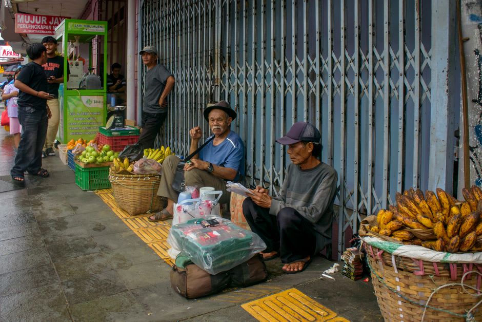 A vendor grilling pisang epe banana over charcoal at a Losari Beach food stall at sunset