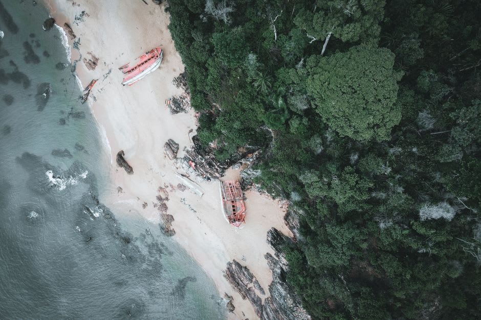 A traditional Mentawai wooden boat pulled up on a white sand beach with dense jungle behind it