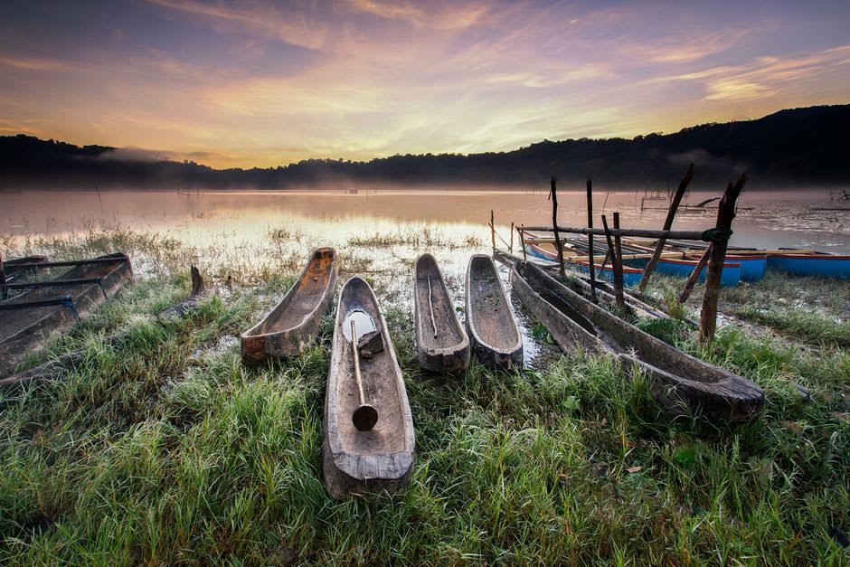 A traditional wooden canoe on the still, mist-covered water of a crater lake at dawn