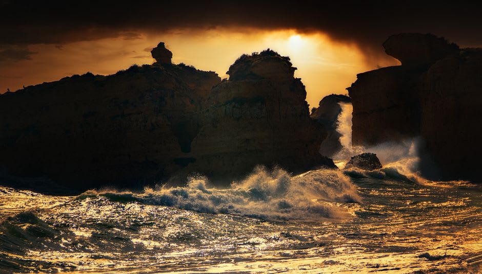Waves crashing against limestone cliffs at sunset with spray catching the golden light