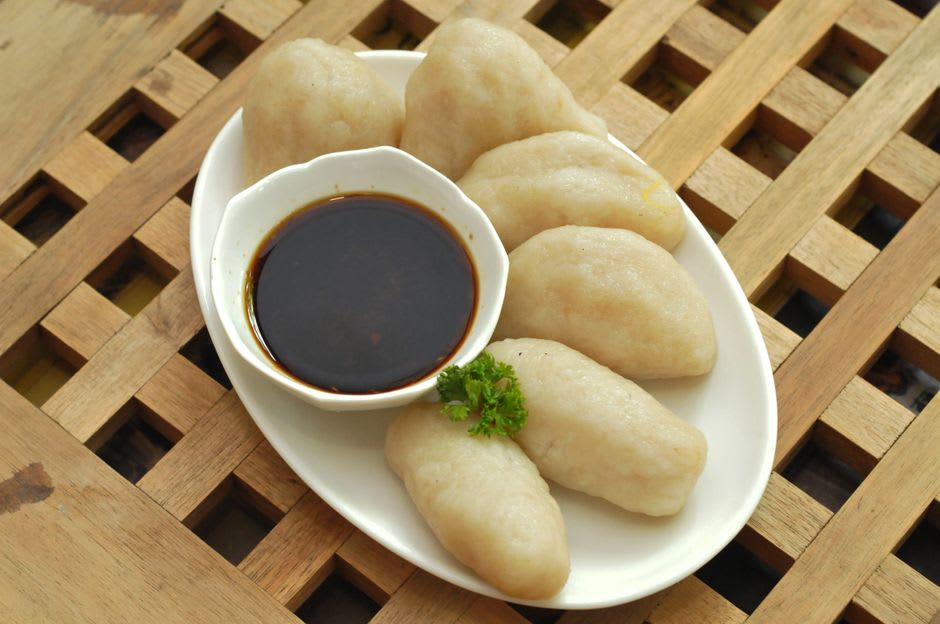 A plate of pempek dumplings served with dark tangy cuko sauce and sliced cucumber
