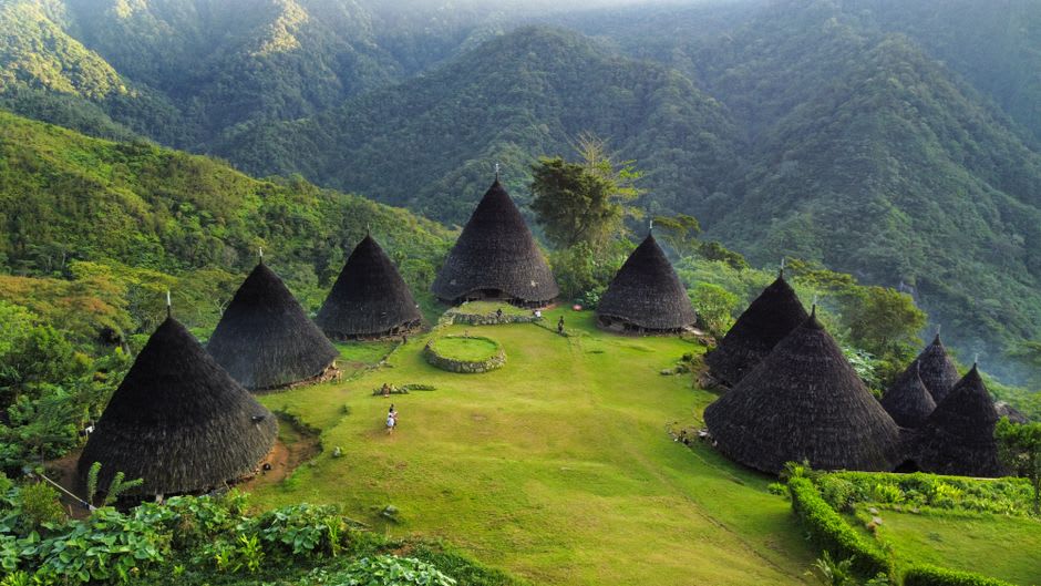Traditional cone-shaped mbaru niang houses on a misty mountainside near Ruteng