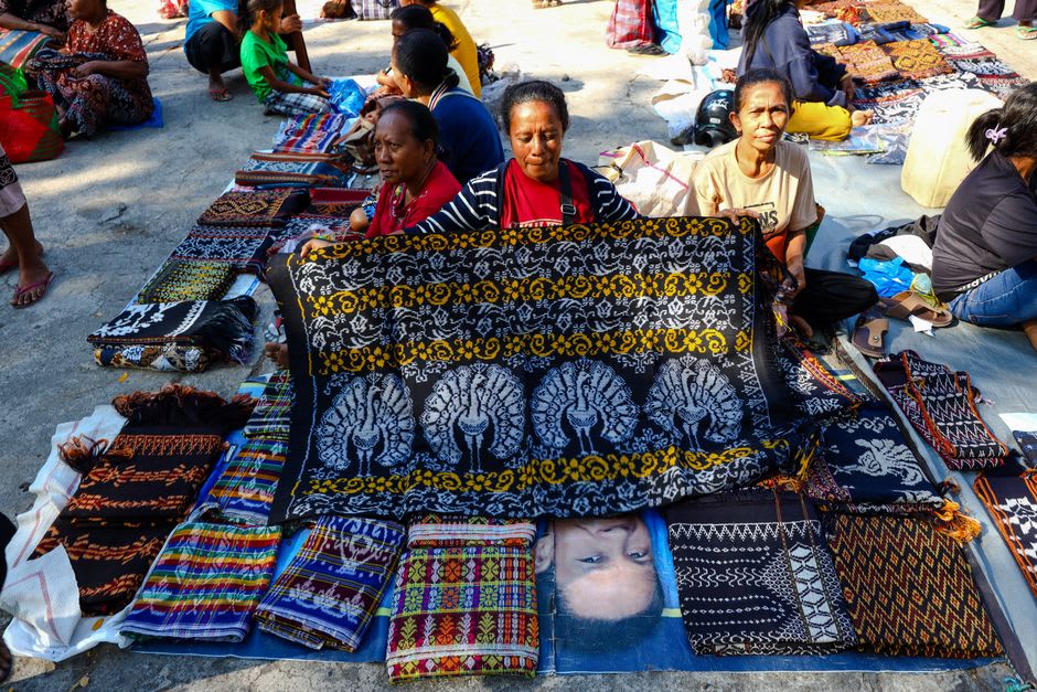 A vendor arranging woven sarung Samarinda textiles at a riverside market stall