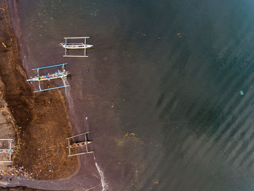 Traditional outrigger fishing boats along Ternate's black volcanic sand shoreline