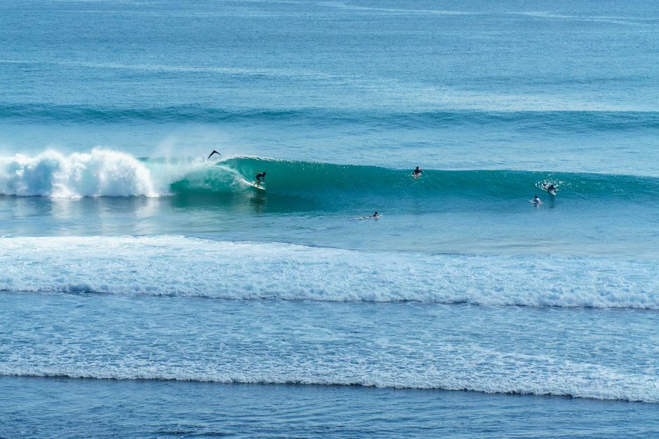 Surfers paddling out through a limestone cave entrance toward a reef break
