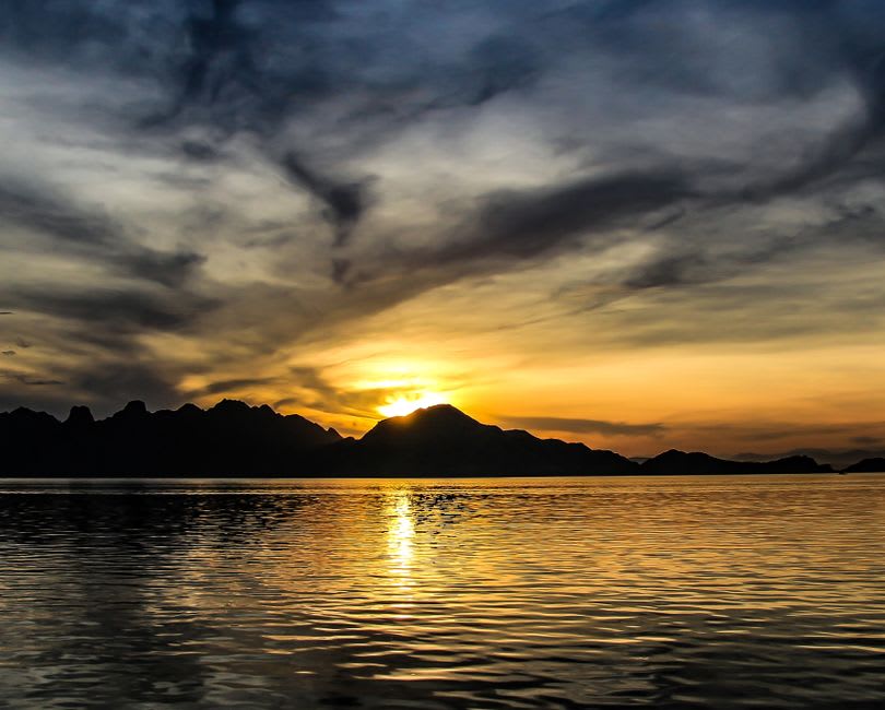 Wooden longboats returning to Waisai harbor at sunset with karst islands in the distance