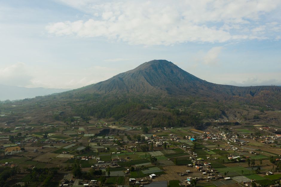 A quiet mountain village street in the Kintamani highlands with volcanic soil visible in the fields
