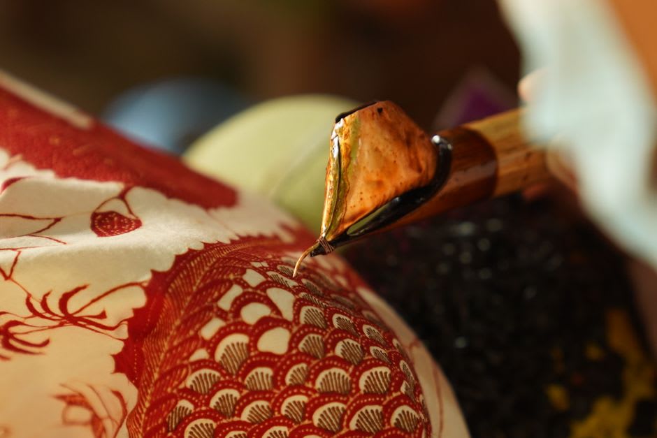 A batik artisan drawing wax patterns onto cloth with a canting pen