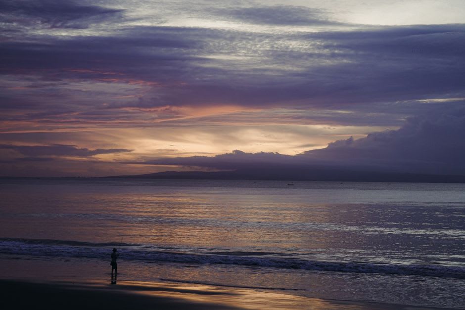Fishing boats and a stone temple silhouette along Sanur's beachfront promenade at dawn