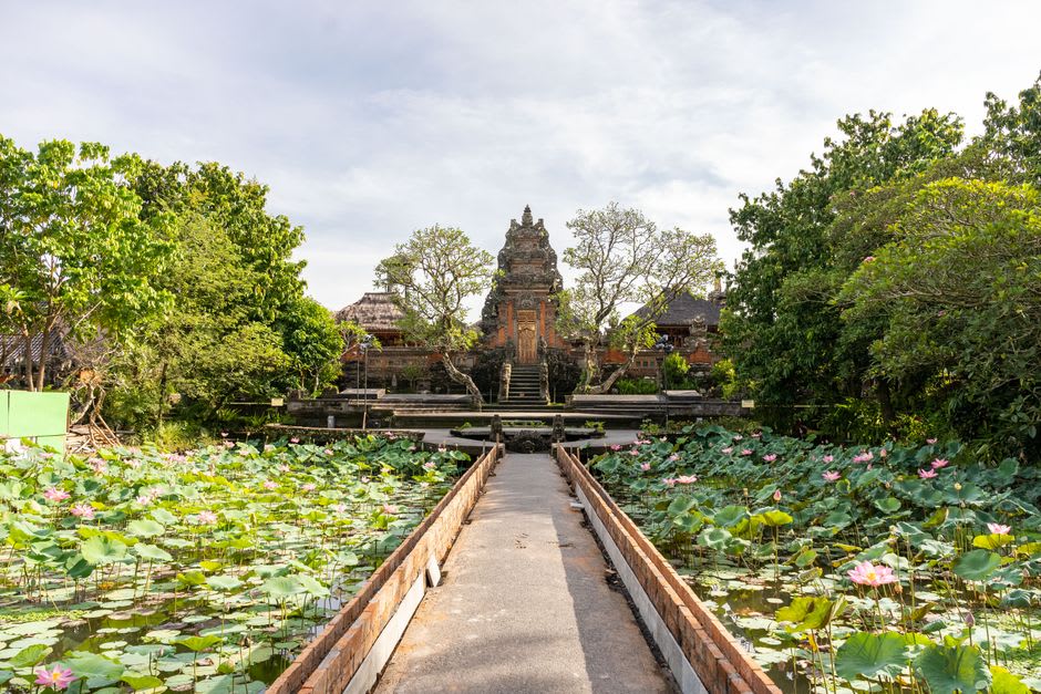 Ornate stone fountain tiers rising from a lily pond at Tirta Gangga surrounded by tropical foliage