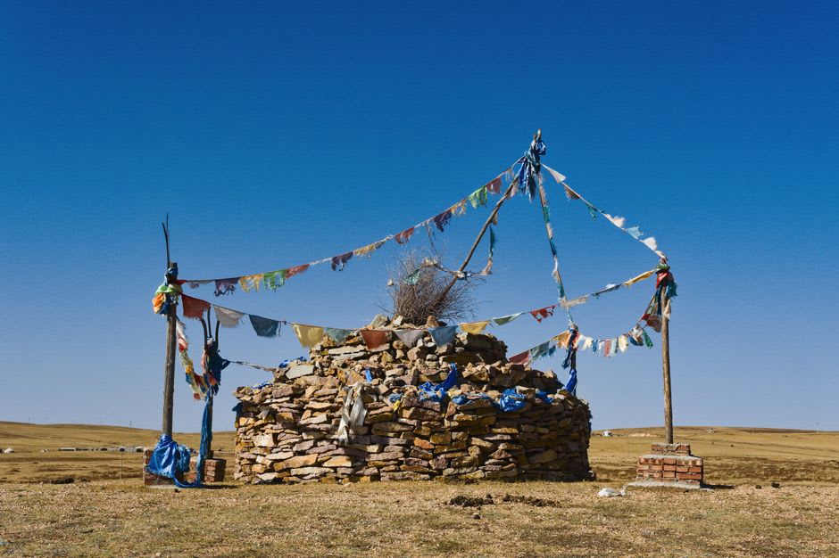 Weathered ovoo shrine cairn draped in blue prayer scarves on the open grassland