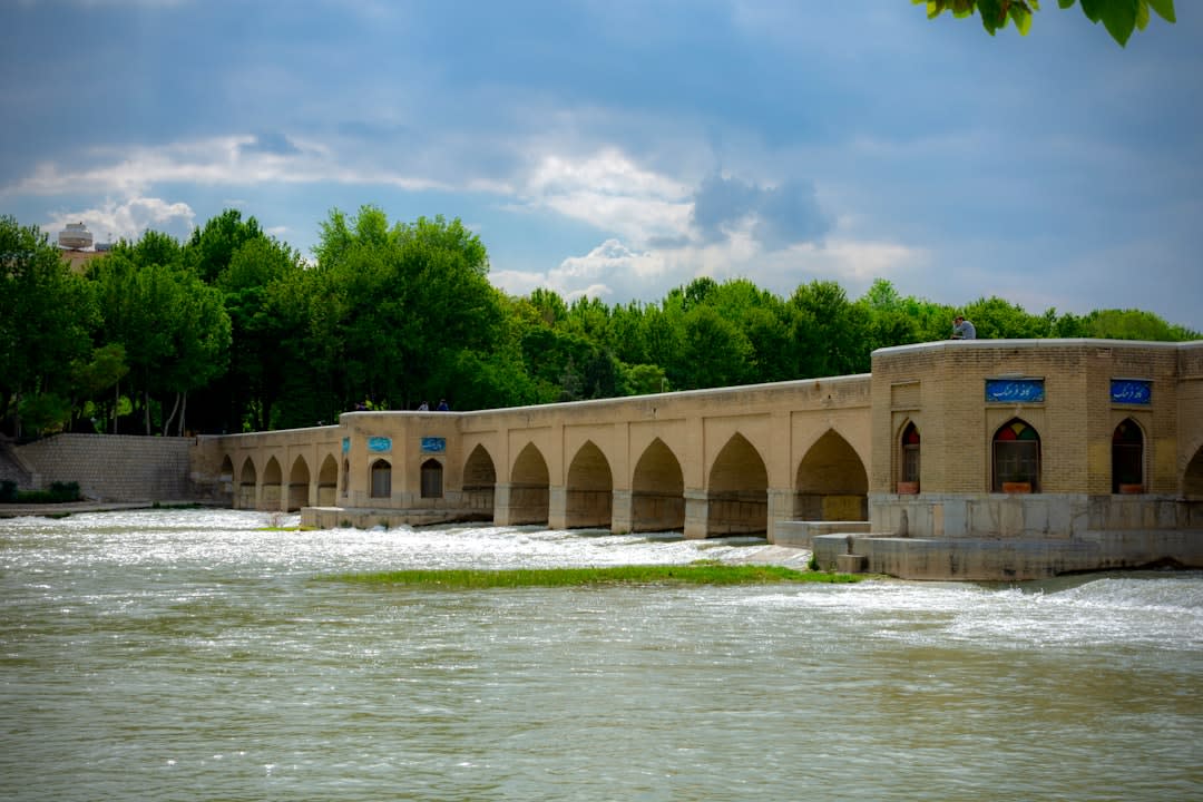 Un claustra en bois sculpté filtrant la lumière sur un mur carrelé à l'intérieur du palais de Hasht Behesht