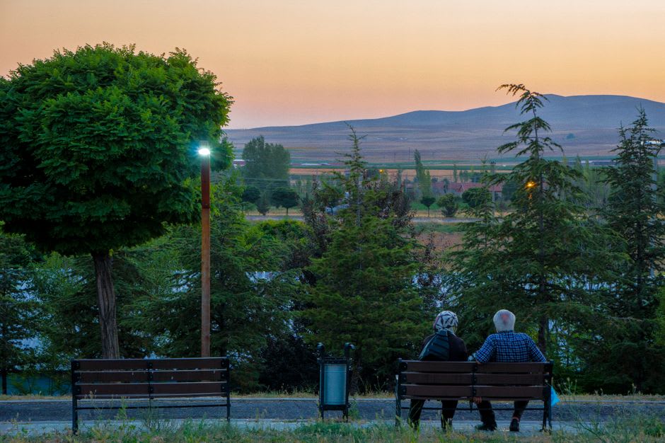 An elderly woman and a young couple sitting near the garden pathways of the Hafez memorial at dusk