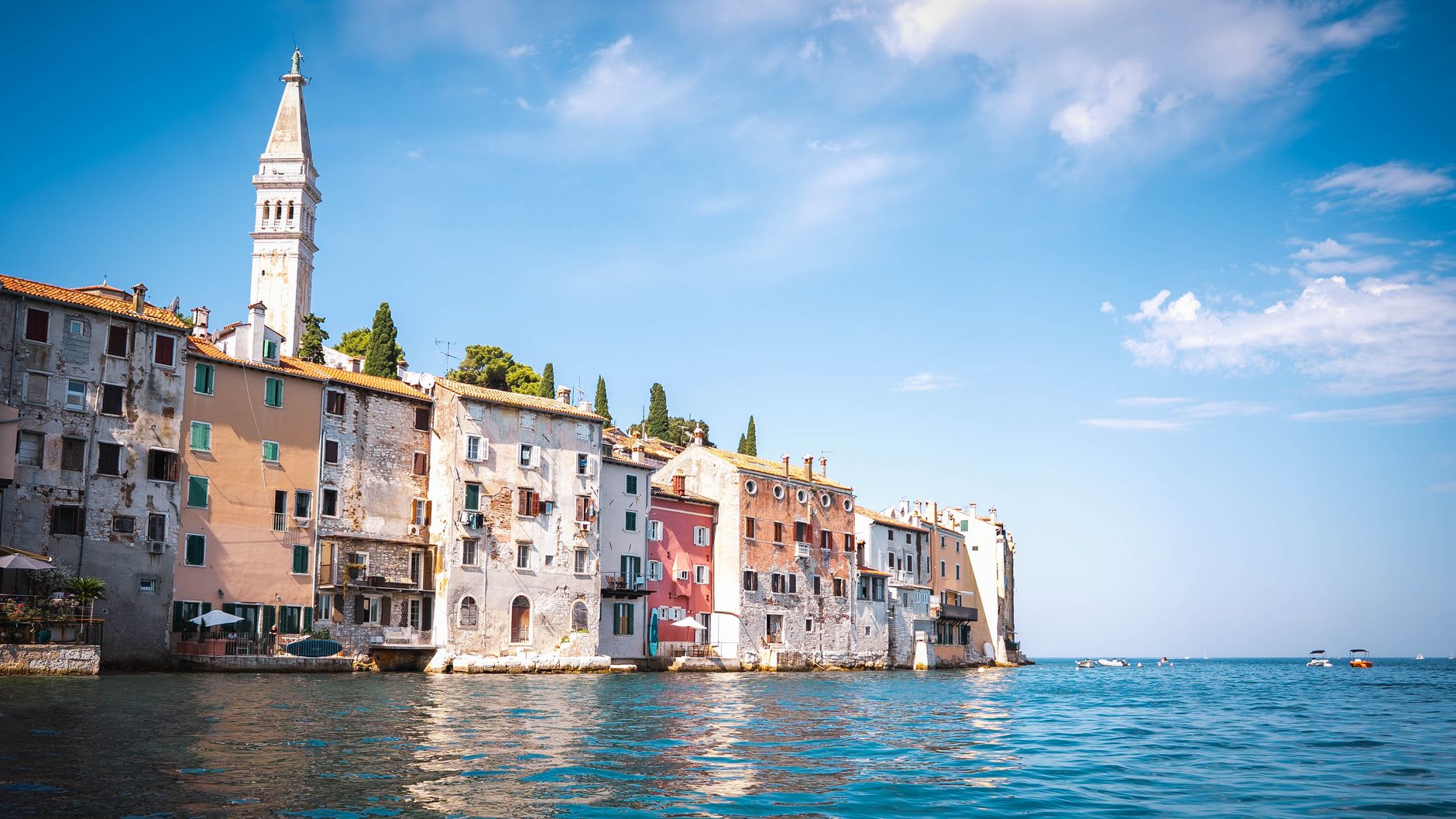 Barcos de pesca reflejados en el agua quieta del puerto de Rovinj al atardecer, edificios iluminados en cálido detrás de ellos