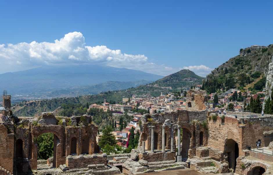 The ancient theater's stone seating with Mount Etna smoking in the distance