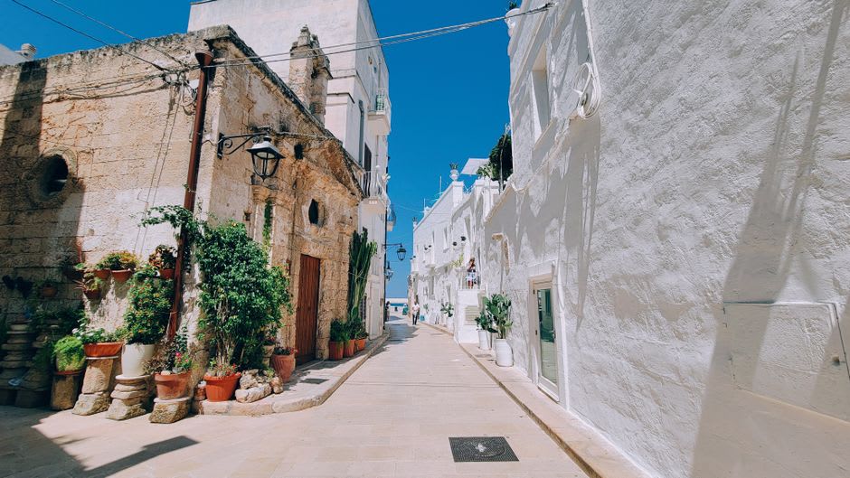 A narrow whitewashed alley in the old town of Ostuni, Puglia, with stone steps and laundry hanging between buildings