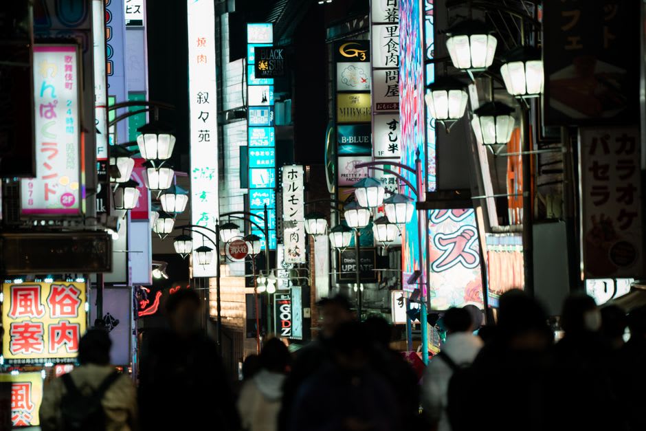 A row of illuminated Kantō lantern poles swaying above the crowd on Akita's main avenue at dusk, each balanced by a single performer