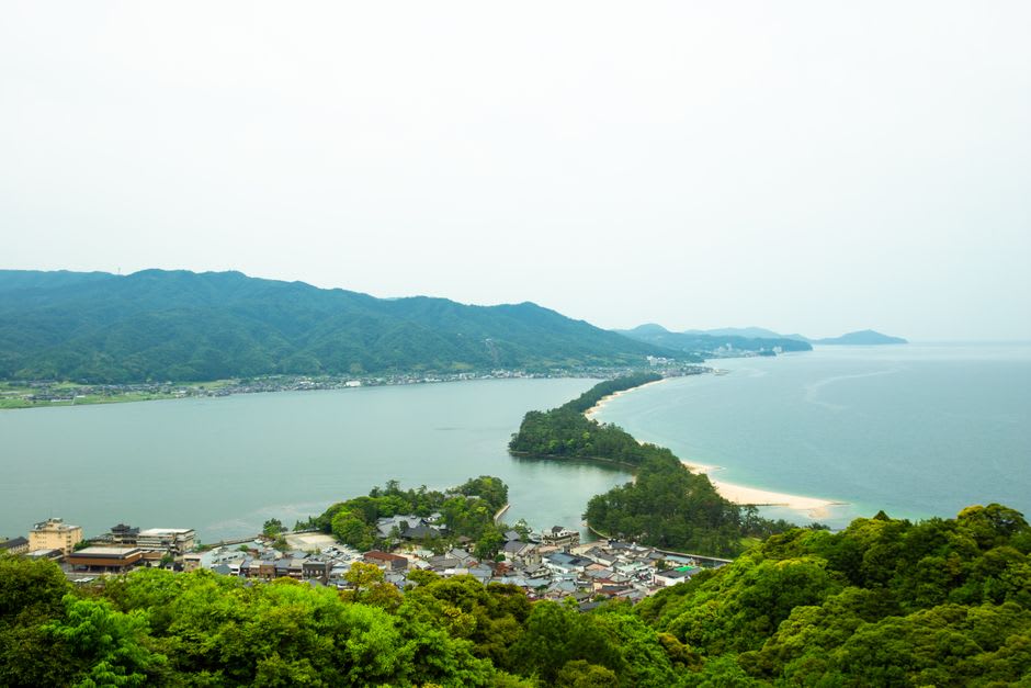 The chairlift climbing the wooded hillside toward Kasamatsu Park, the blue bay and sandbar spread out below