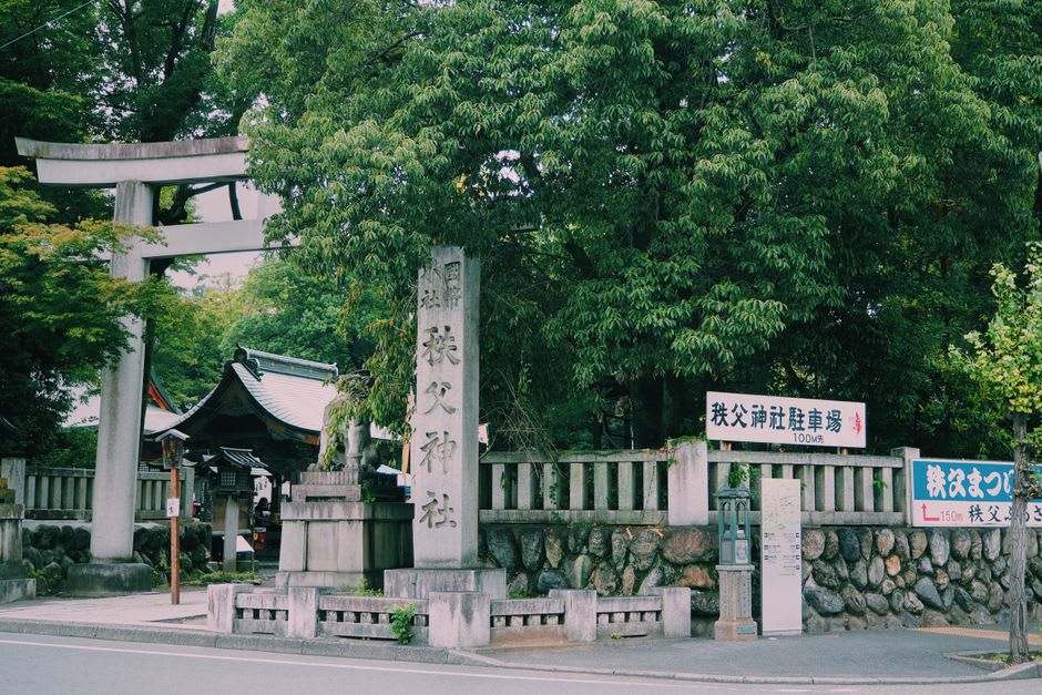 The intricately carved main hall of Chichibu Shrine, dark wood eaves painted with dragons and figures beneath a heavy tiled roof