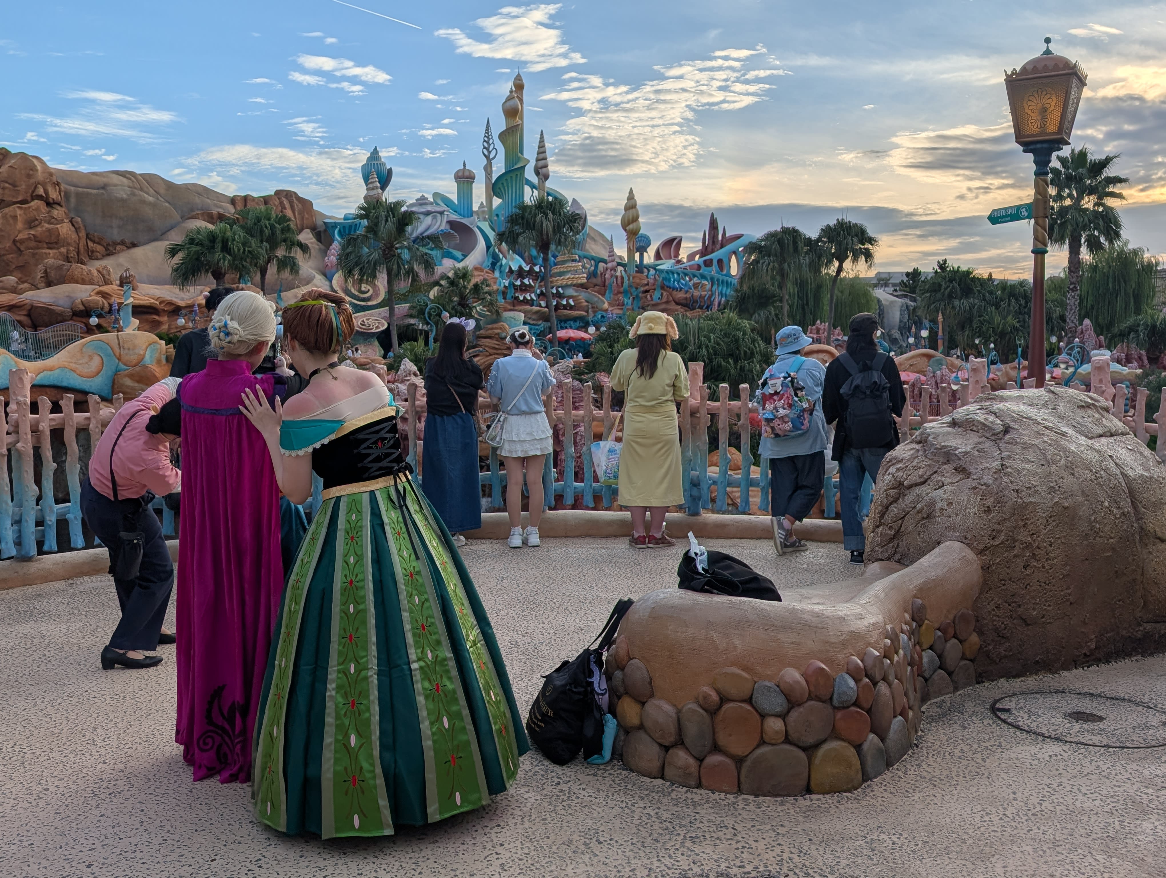 A visitor in a full Anna coronation gown gazing at the Fantasy Springs castle at golden hour — cosplay as devotion, the park and its visitors becoming one