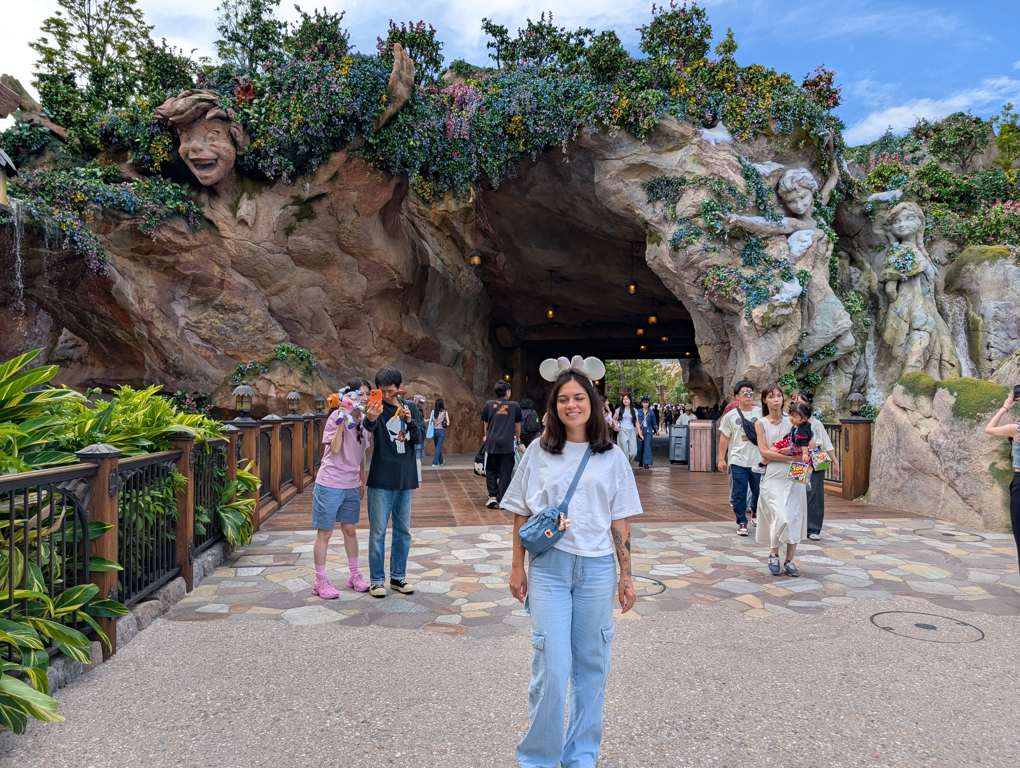 Lia at the Fantasy Springs entrance — towering rock sculptures of faces and vines rising behind her, visitors streaming through the archway into the new world beyond