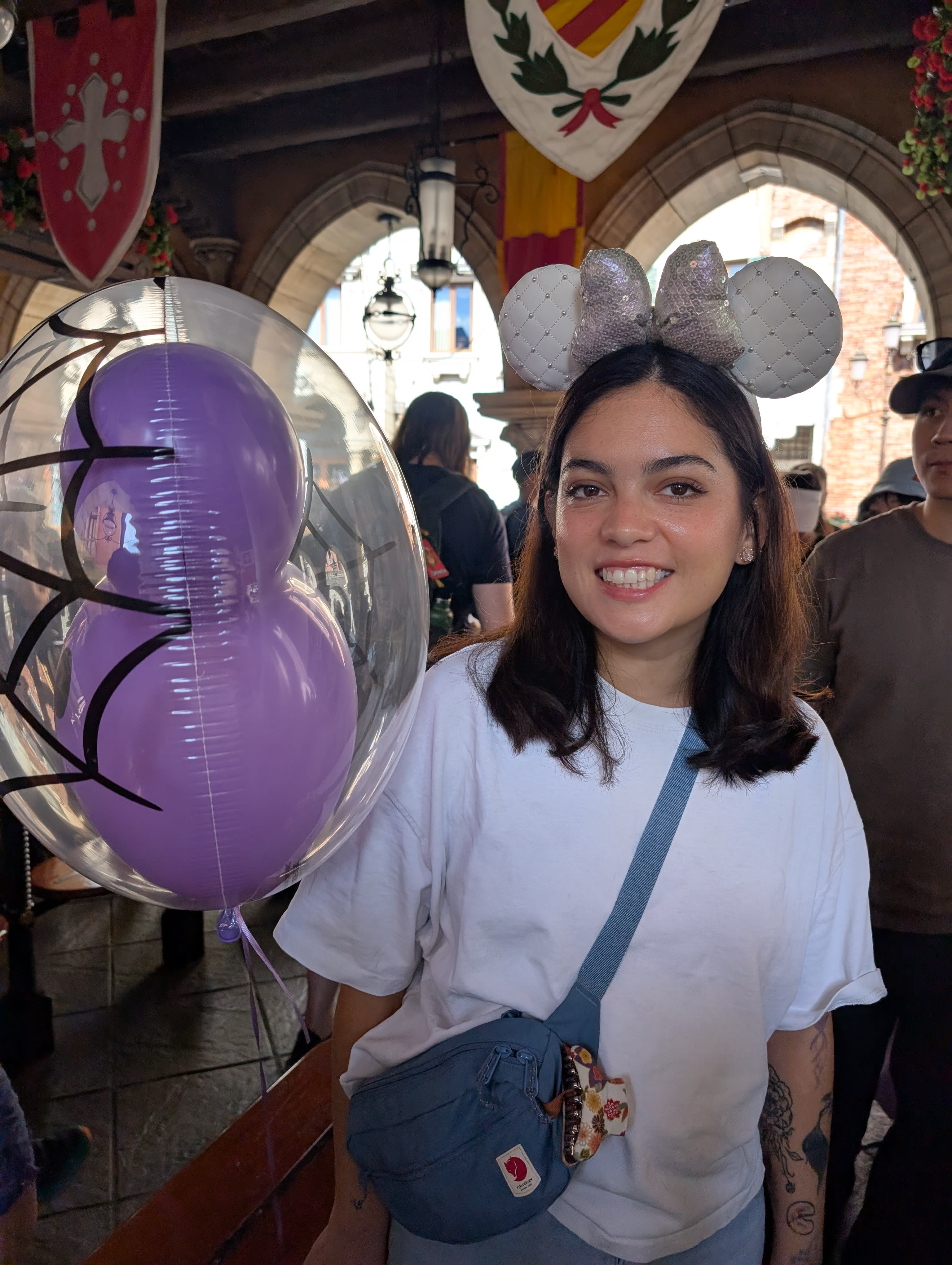 Lia with Minnie ears and a Halloween balloon under a medieval archway at DisneySea — smiling with the sincerity the park demands