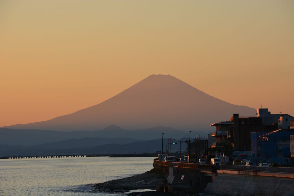 A narrow climbing street on Enoshima lined with seafood stalls and a vermilion shrine gate, steam rising from grills
