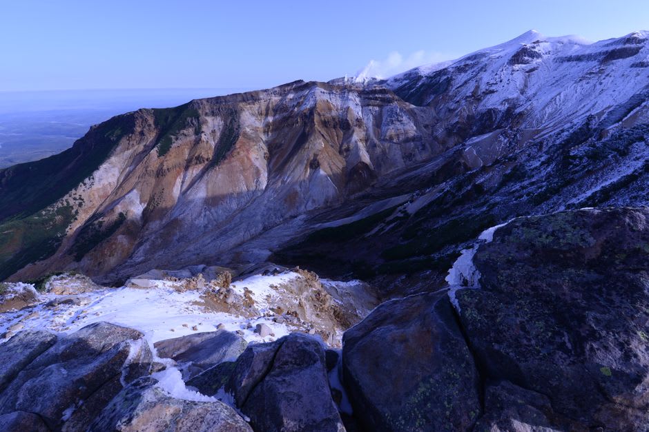 Boardwalks crossing the alpine marshland of Hachimantai past a round crater pond, dwarf pine and distant ridges under a wide sky