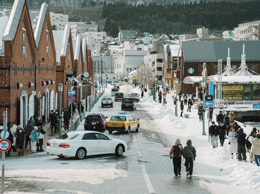A steep Motomachi street in Hakodate lined with pale nineteenth-century Western buildings, the blue harbor visible at the bottom of the slope