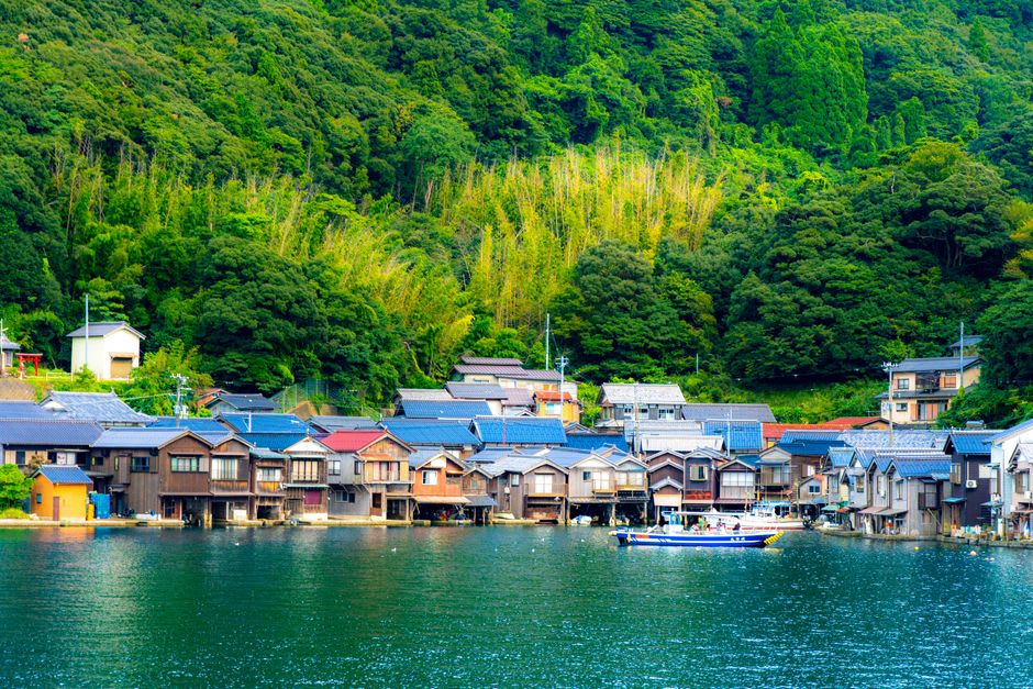 View from a boat of the unbroken wall of funaya boat houses reflected in the calm water of Ine Bay