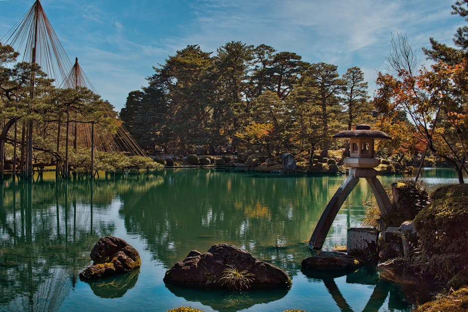 Kenroku-en garden with its iconic stone lantern beside the tranquil pond, sculpted pines reflected in the still water
