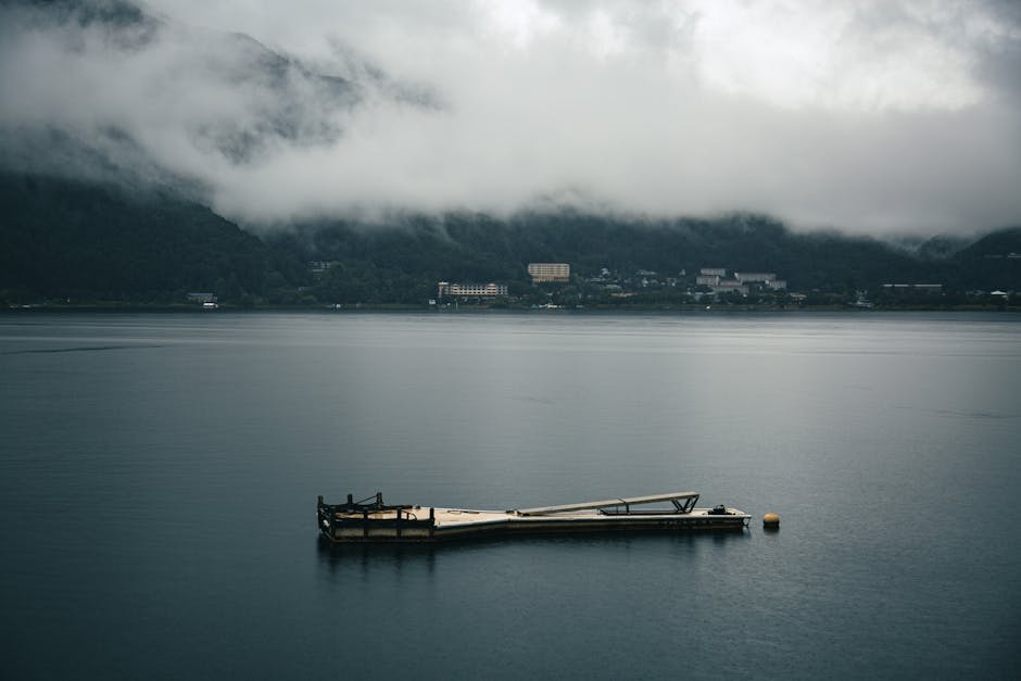 Lake Kawaguchiko shrouded in morning mist, the mountains rising as dark silhouettes behind the still water and the floating dock