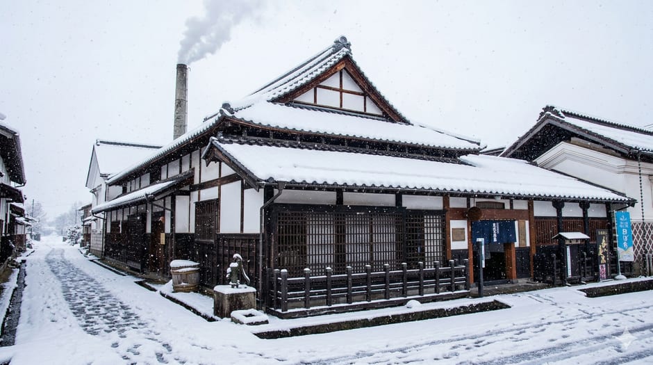 Black-plastered clay kura storehouse standing on a quiet residential corner in Kitakata