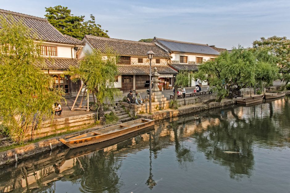 A denim workshop in Kurashiki, indigo-dyed fabric and finished jeans hanging on wooden racks, deep blue tones filling the frame