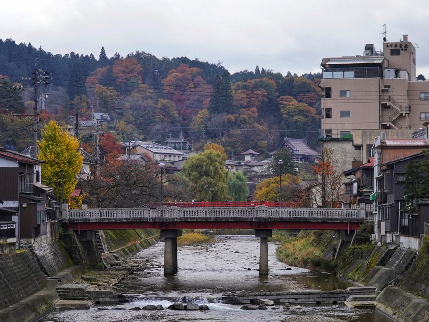 A lantern-lit stone lane in Kurokawa Onsen at night, warm light glowing on wooden ryokan walls beside the river