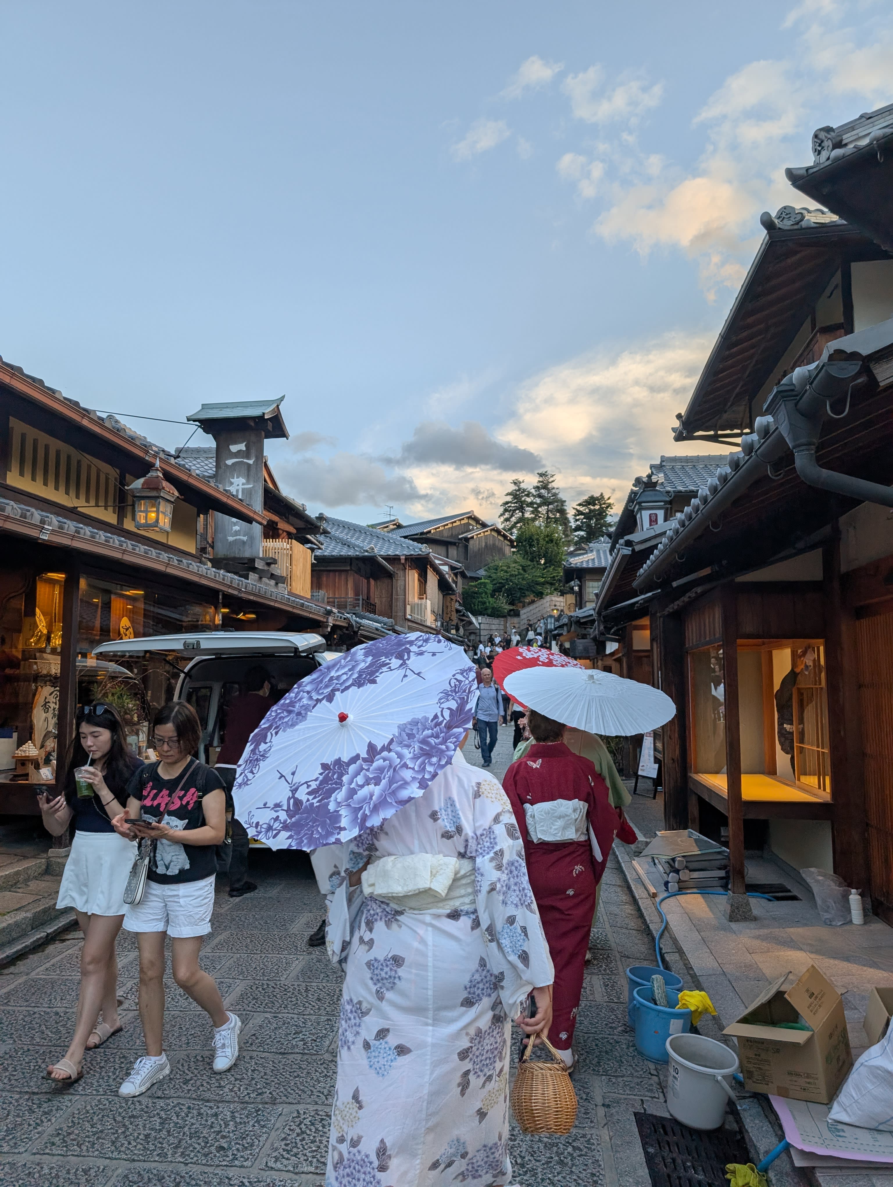 Women in kimonos walking the stone-paved lanes of Sannenzaka at dusk — the wooden shopfronts glowing, the sky turning gold