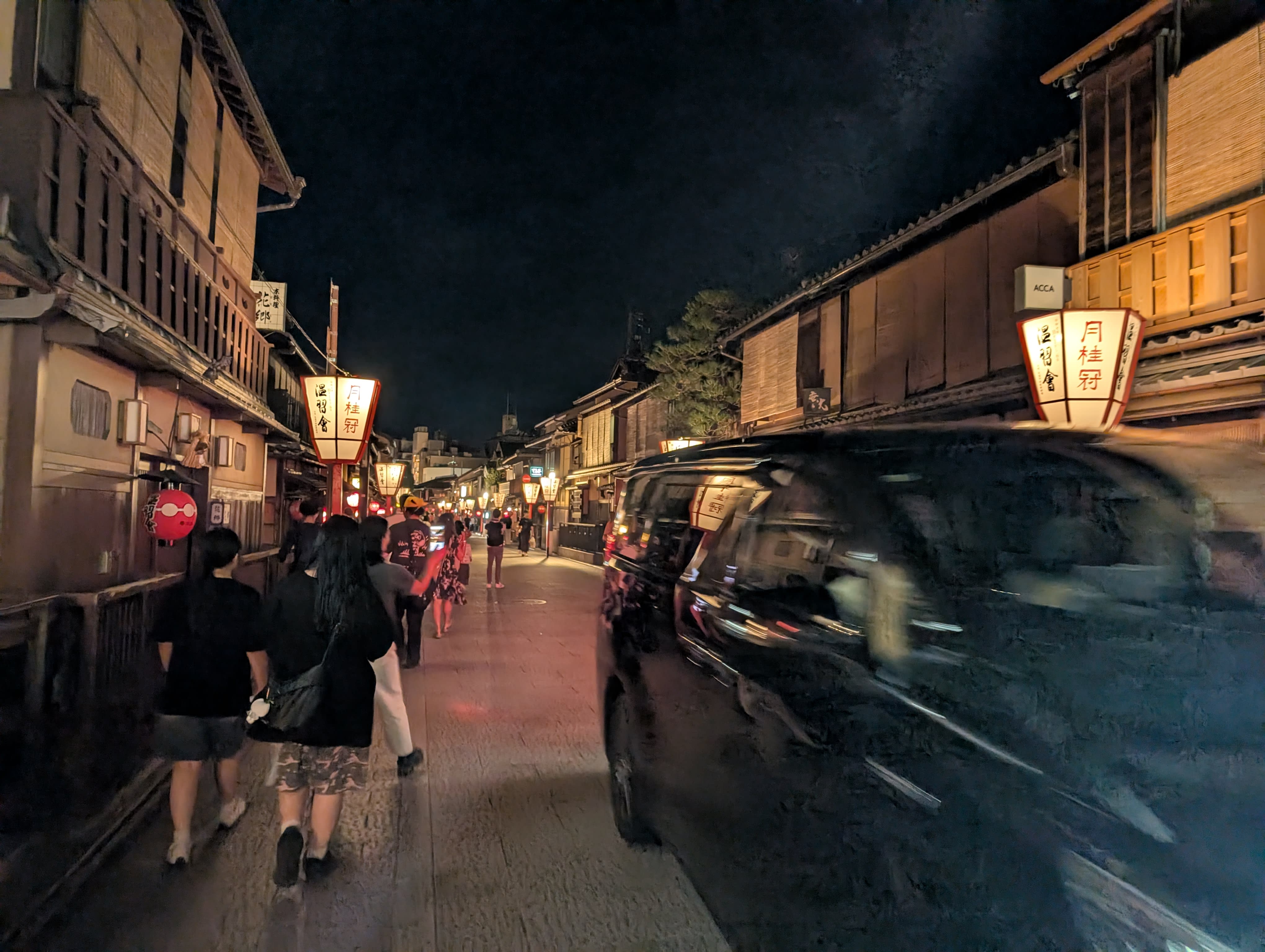 Gion at night — lanterns glowing on wooden façades, figures walking through the warm amber light of Kyoto's geisha district