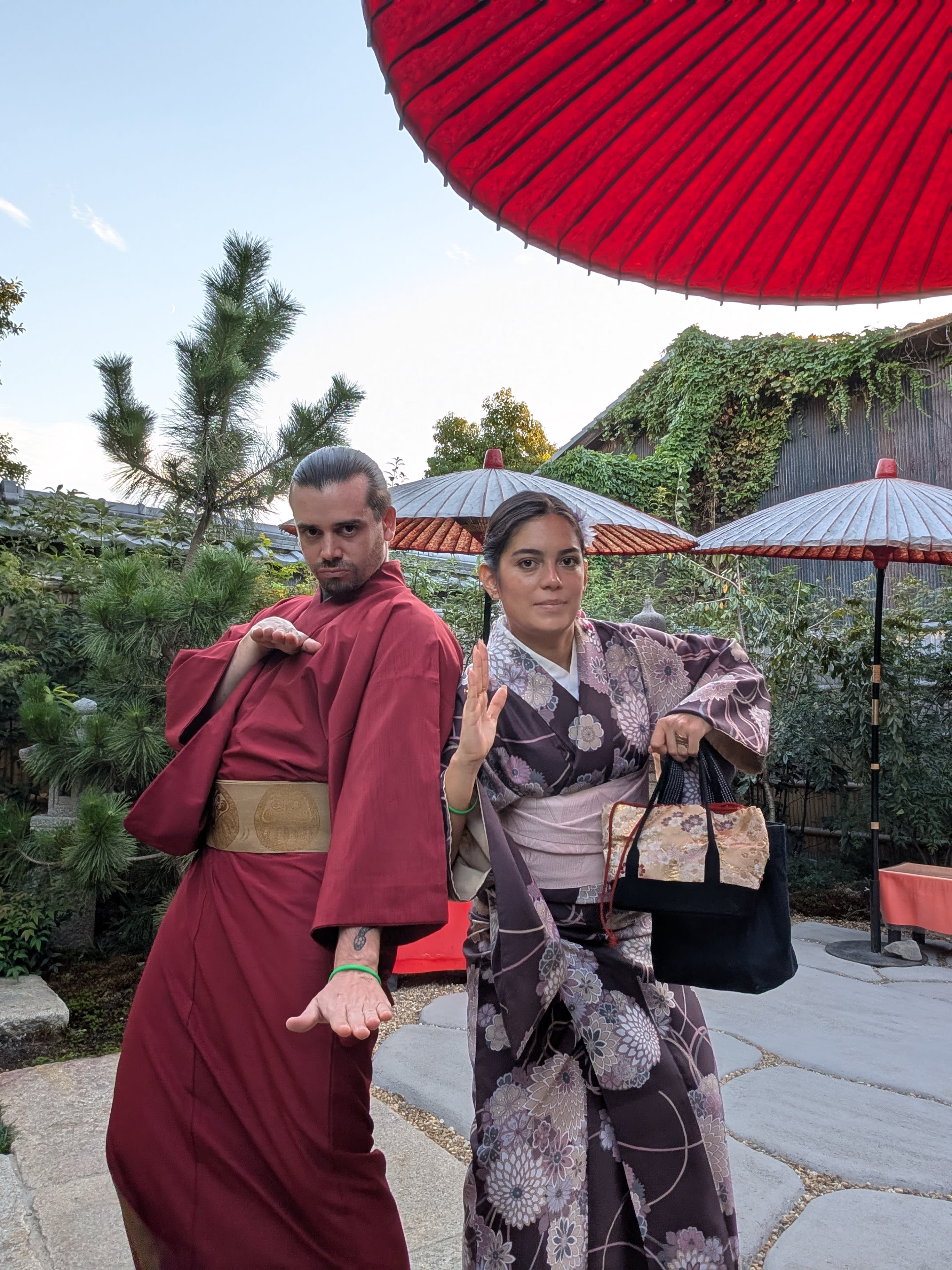 Pierre and Lia in full kimonos outside the tea house — Pierre in deep red, Lia in a dark floral pattern, posing with the confidence of people who have no idea how to sit down in these clothes