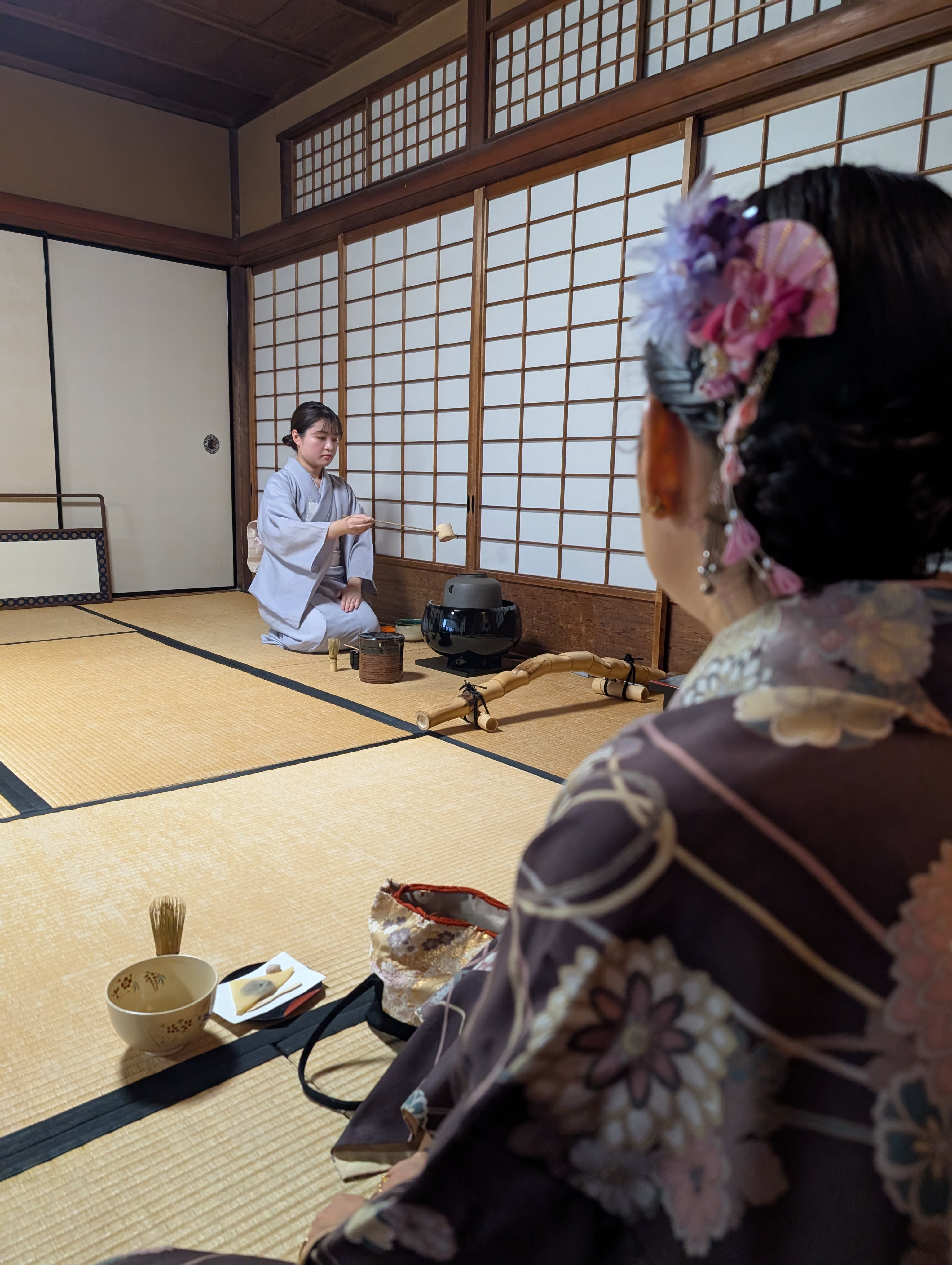 The tea ceremony — our tea master in a pale blue kimono kneeling on tatami, whisking matcha with quiet precision, Lia watching from across the room
