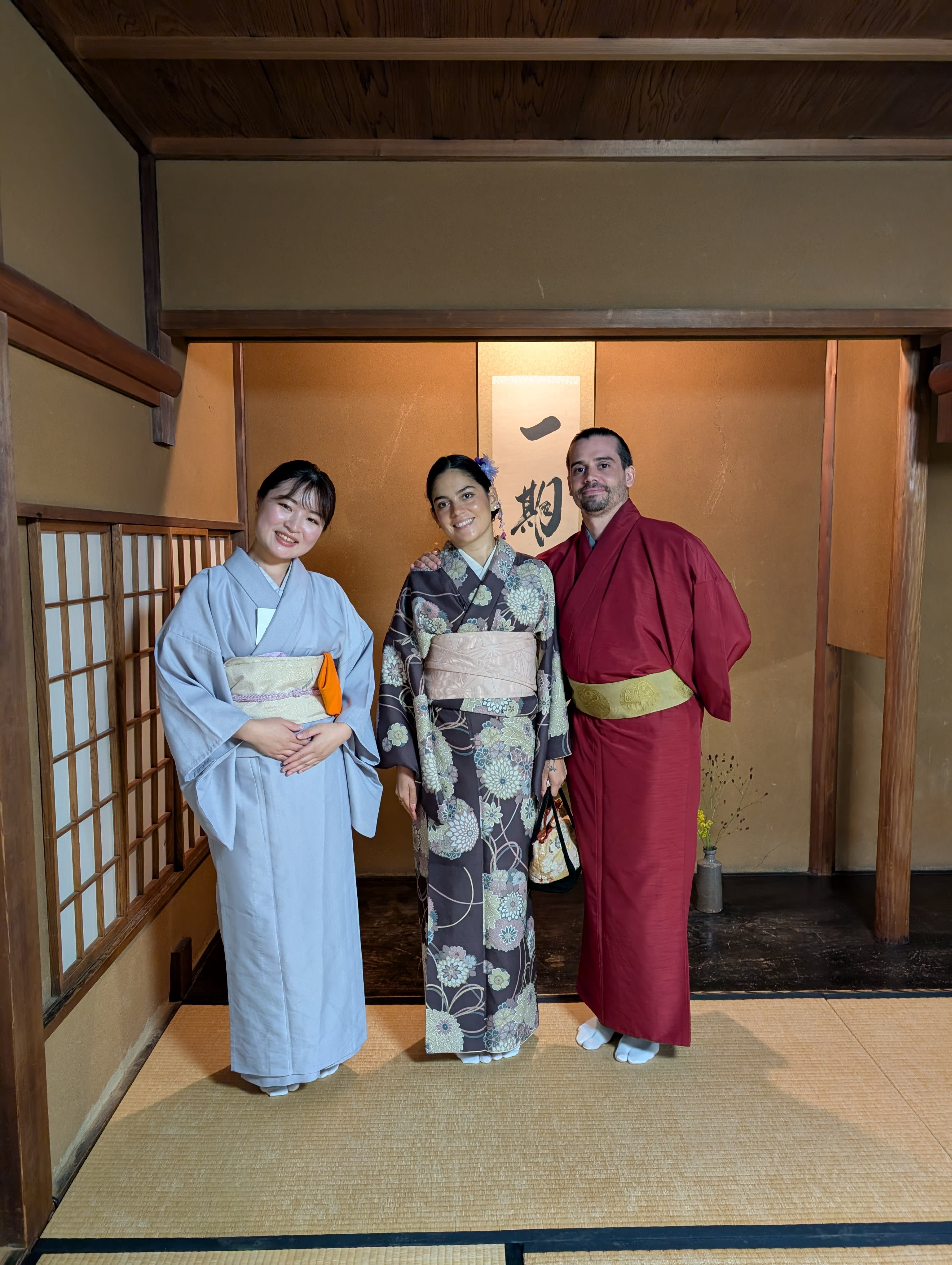 Pierre, Lia, and our tea master standing together on the tatami — three kimonos, a calligraphy scroll behind us, the quiet warmth of shared ritual
