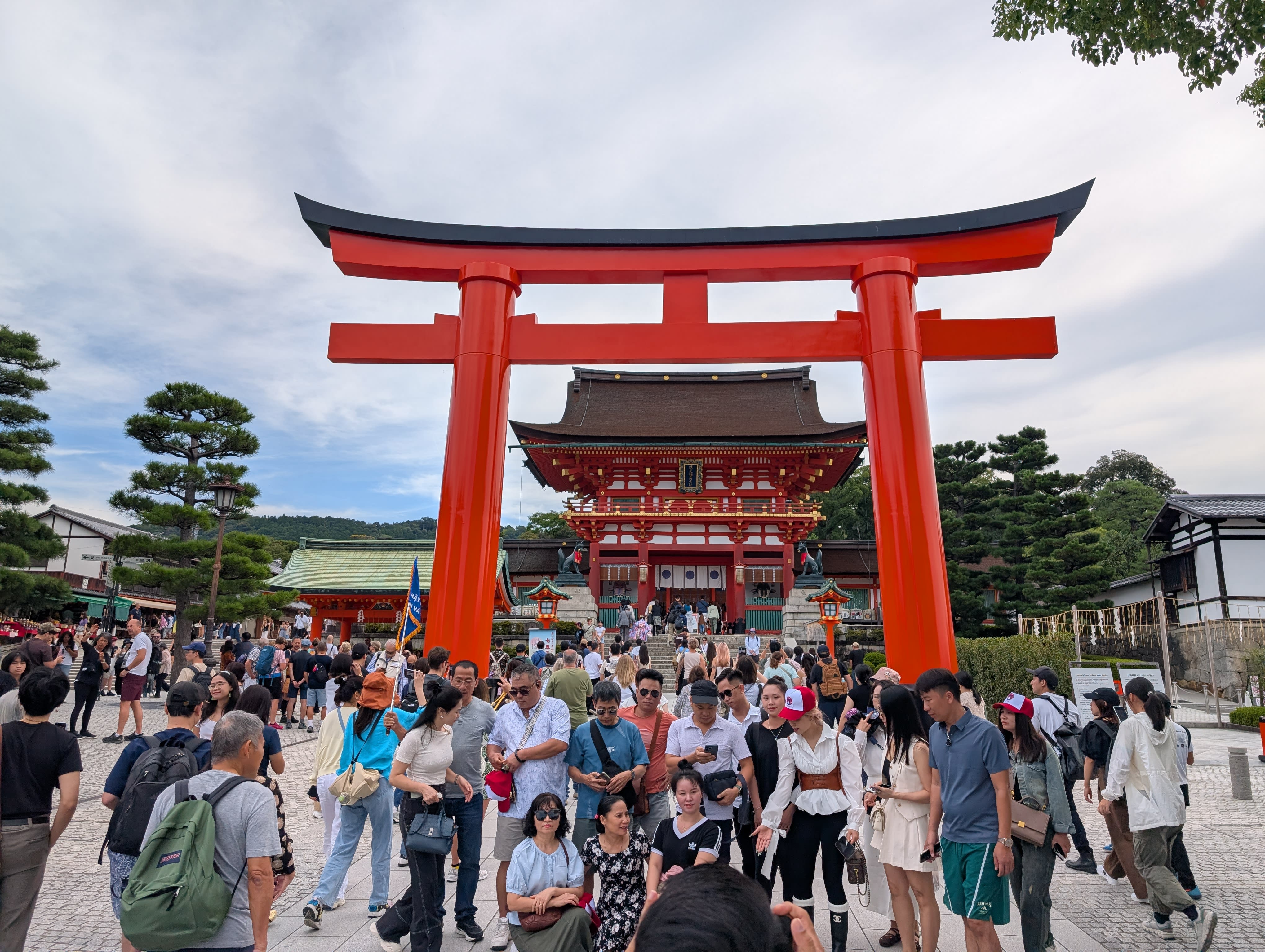 The main entrance to Fushimi Inari Taisha — the massive red torii gate framing the ornate Rōmon gate, the crowds already gathering beneath it