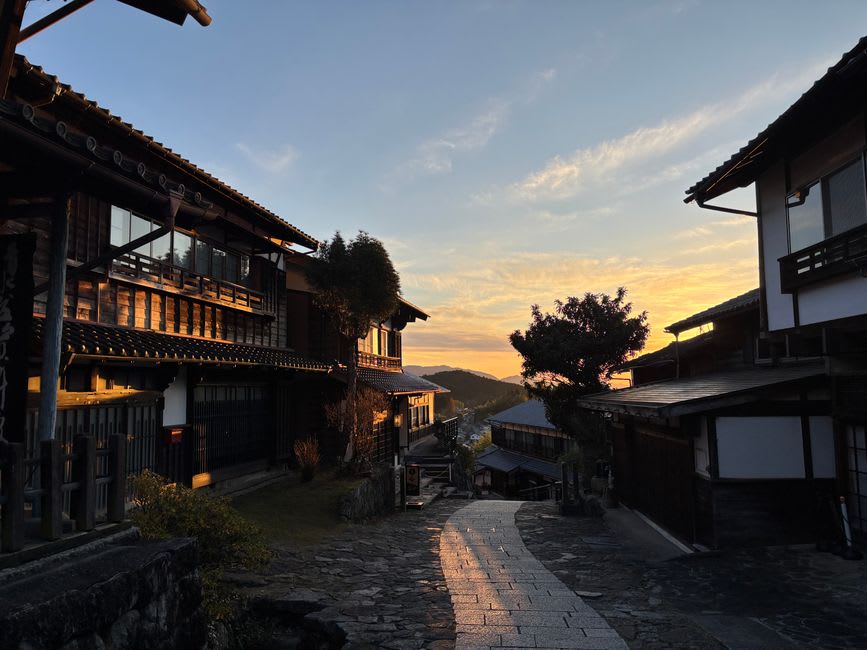 Magome's stone-paved main street climbing steeply between dark wooden shopfronts, a moss-edged water channel running down one side