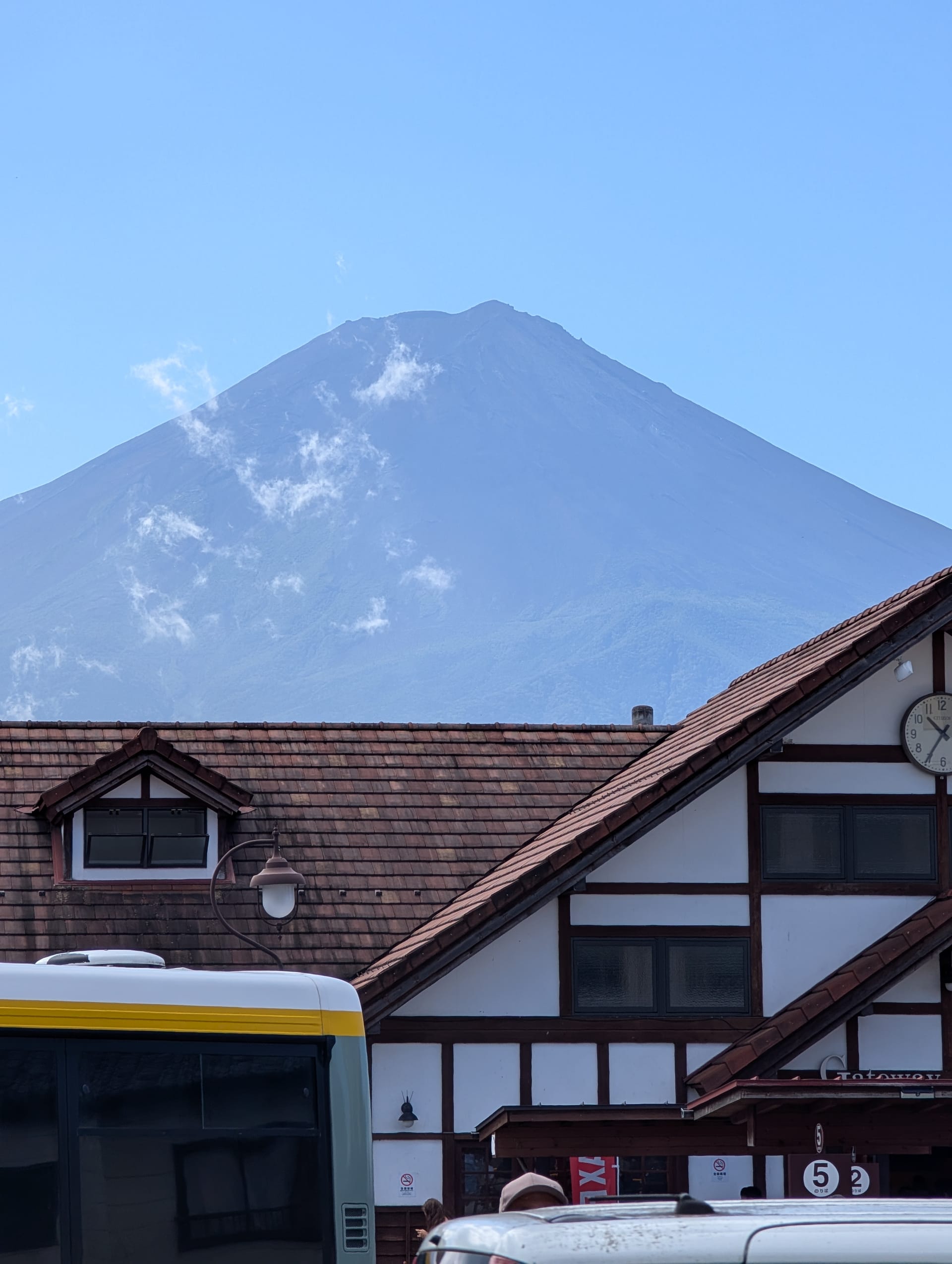 Mt. Fuji rising above the rooftops near Kawaguchiko Station, hazy against a blue sky