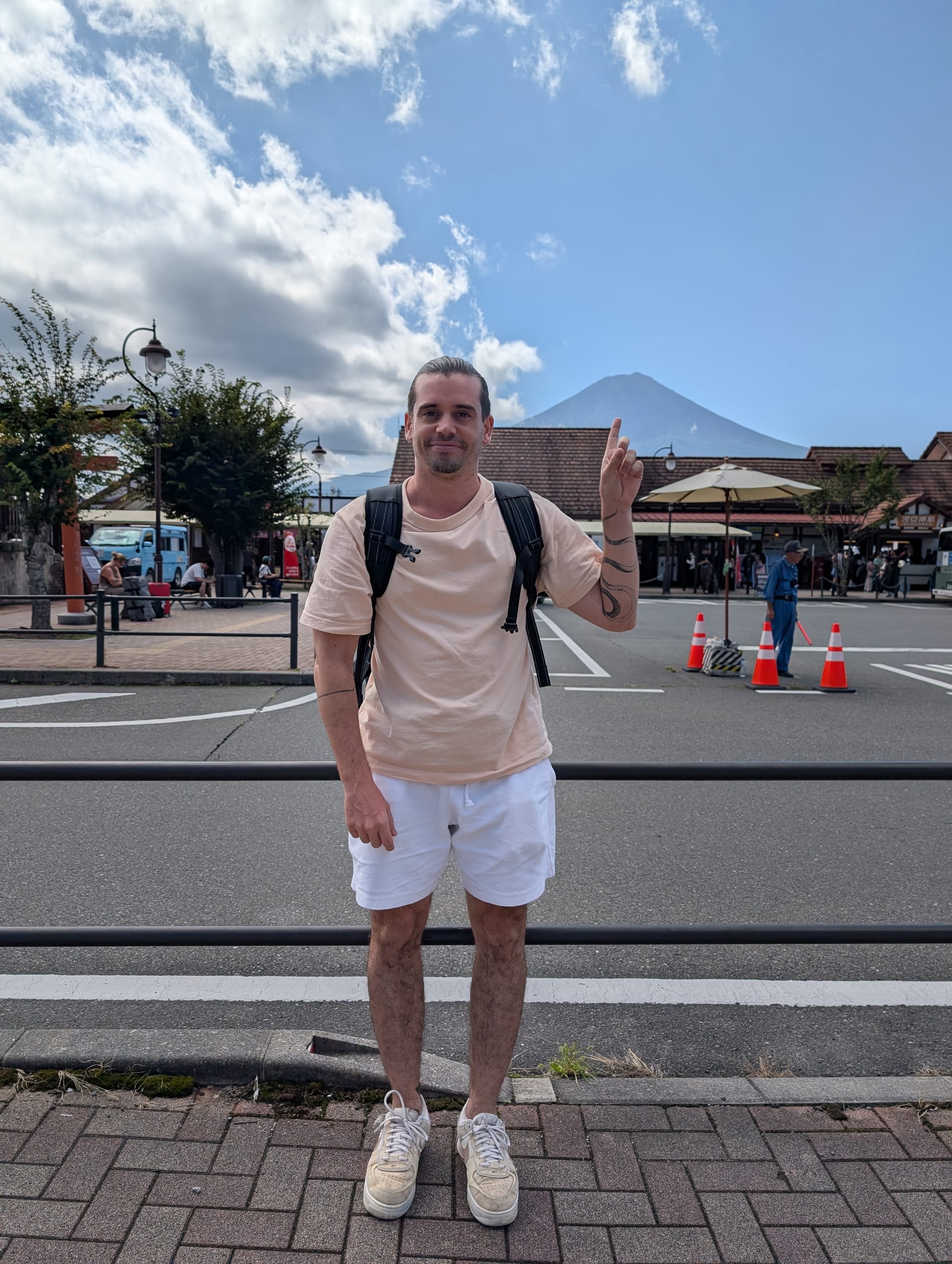 Pierre standing outside Kawaguchiko Station, pointing at Mt. Fuji rising behind the buildings