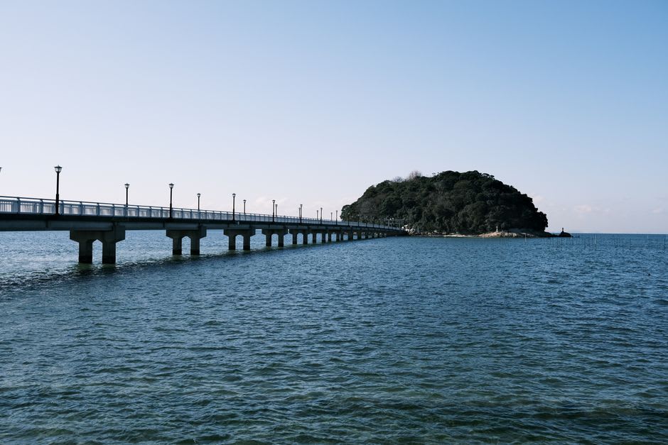 Muroran's industrial harbor at night, refineries and steelworks glittering with white and amber lights, steam rising, the Hakuchō Bridge arcing above the dark water