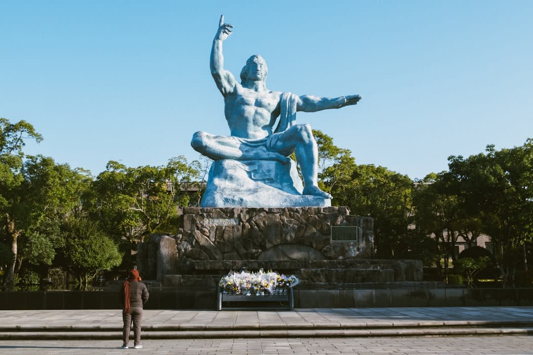 The black stone pillar marking the hypocenter in Nagasaki's Peace Park, flowers laid at its base under a grey sky