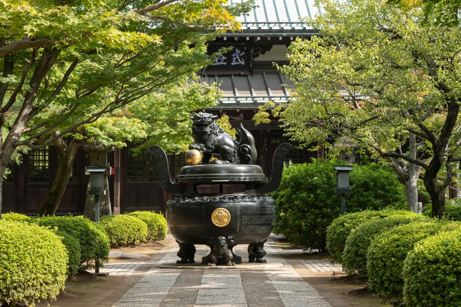 A quiet side lane in old Narita with weathered wooden houses, a stone lantern, and a small local shrine tucked among them